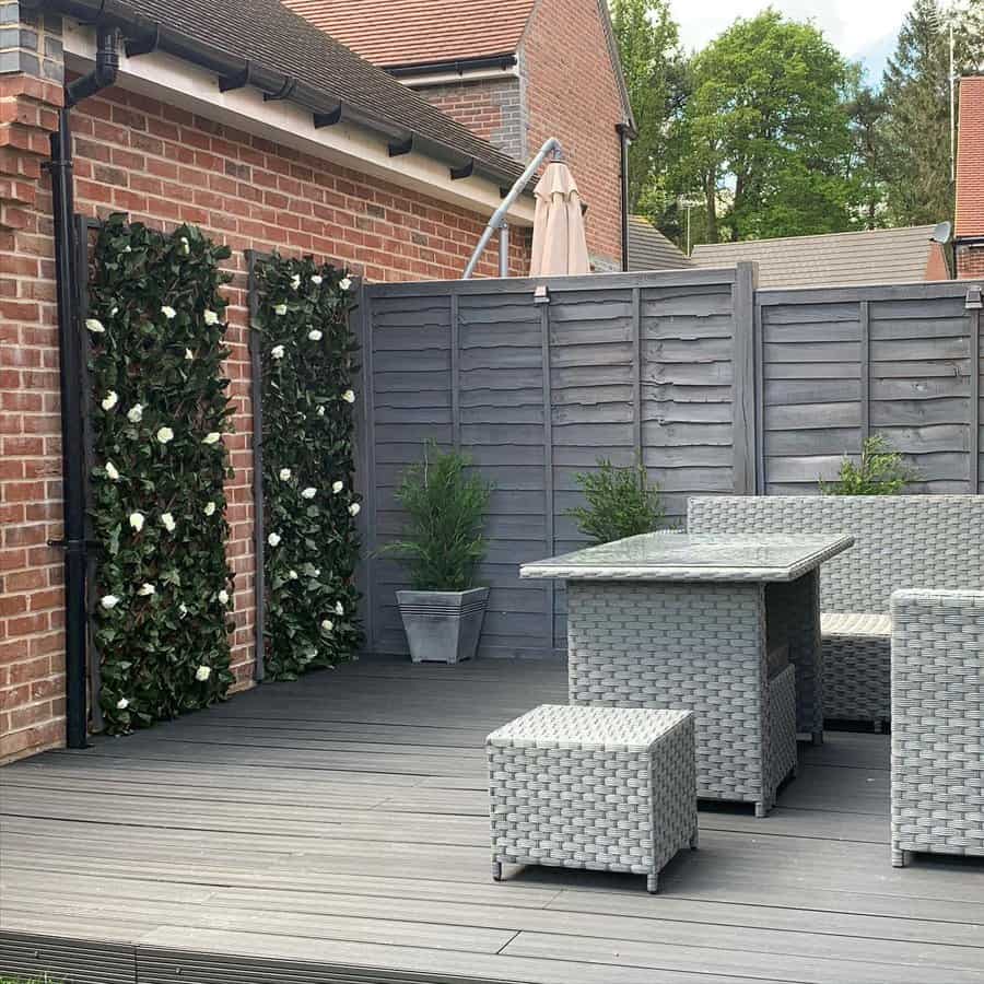 Rooftop patio with gray wicker furniture, gray wooden flooring, and artificial vertical green plant panels on the brick wall