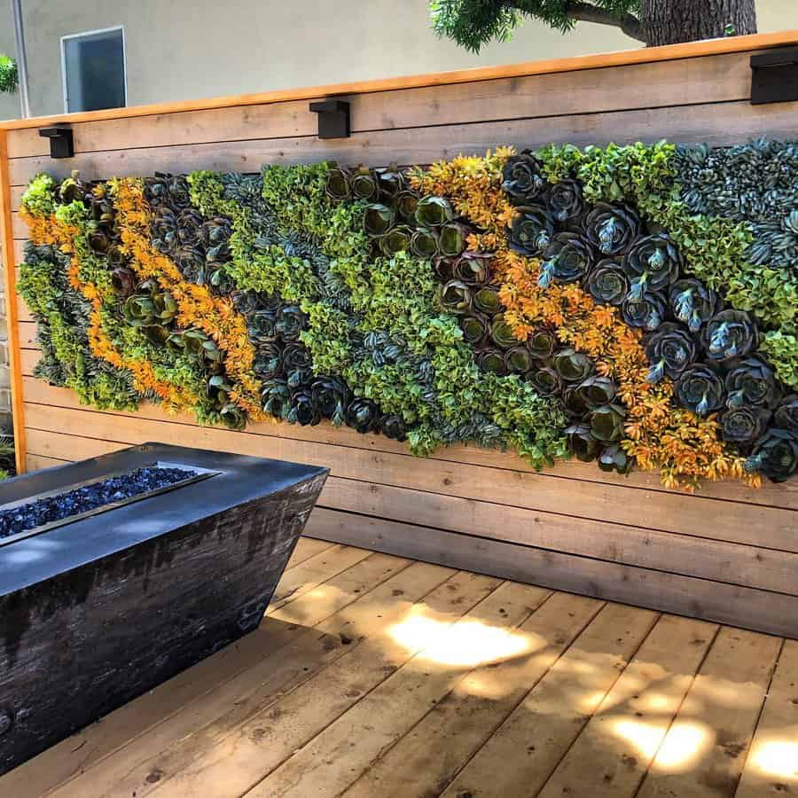 Vertical garden with green and yellow plants on a wooden wall by a raised rectangular planter on a wooden deck