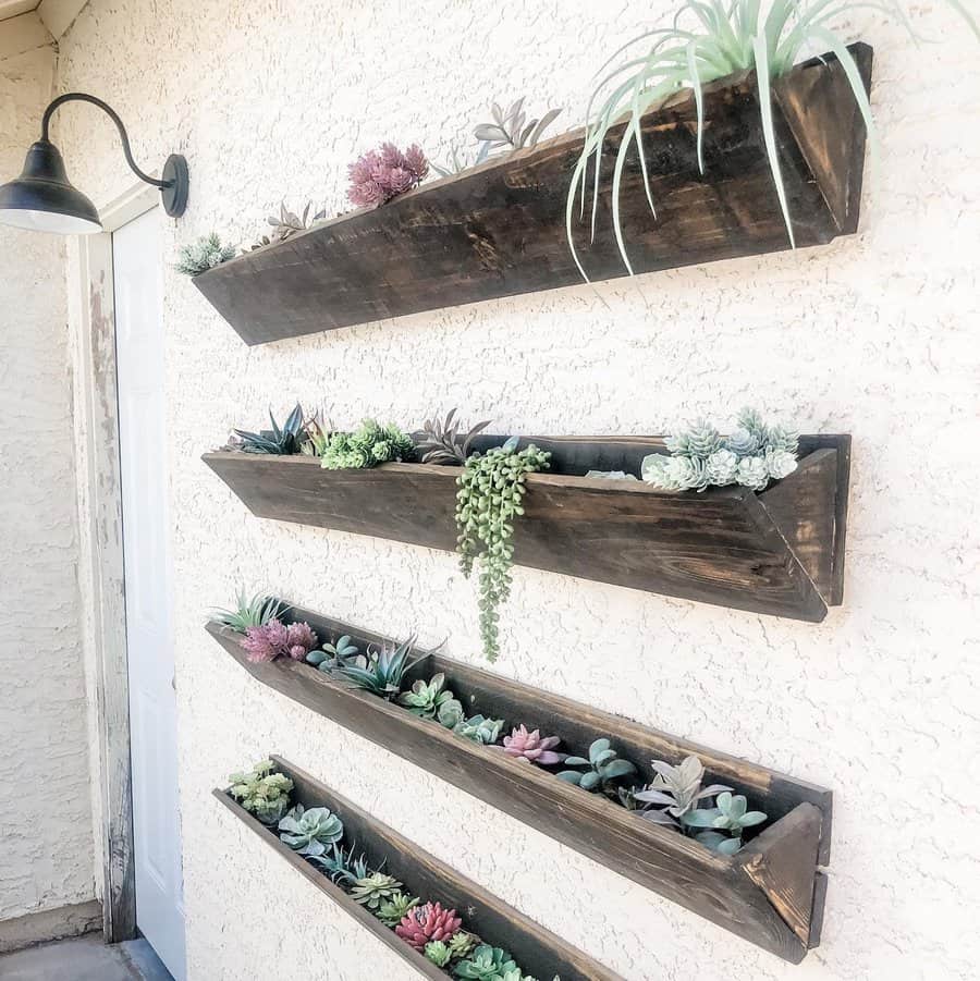 Wooden wall planters filled with various succulents, mounted on a textured wall under a black outdoor light fixture