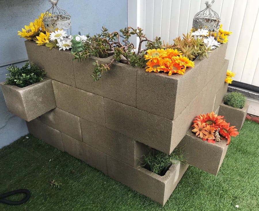 Tiered cinder block planter filled with colorful flowers and succulents, featuring built-in side pockets for greenery, set on artificial grass