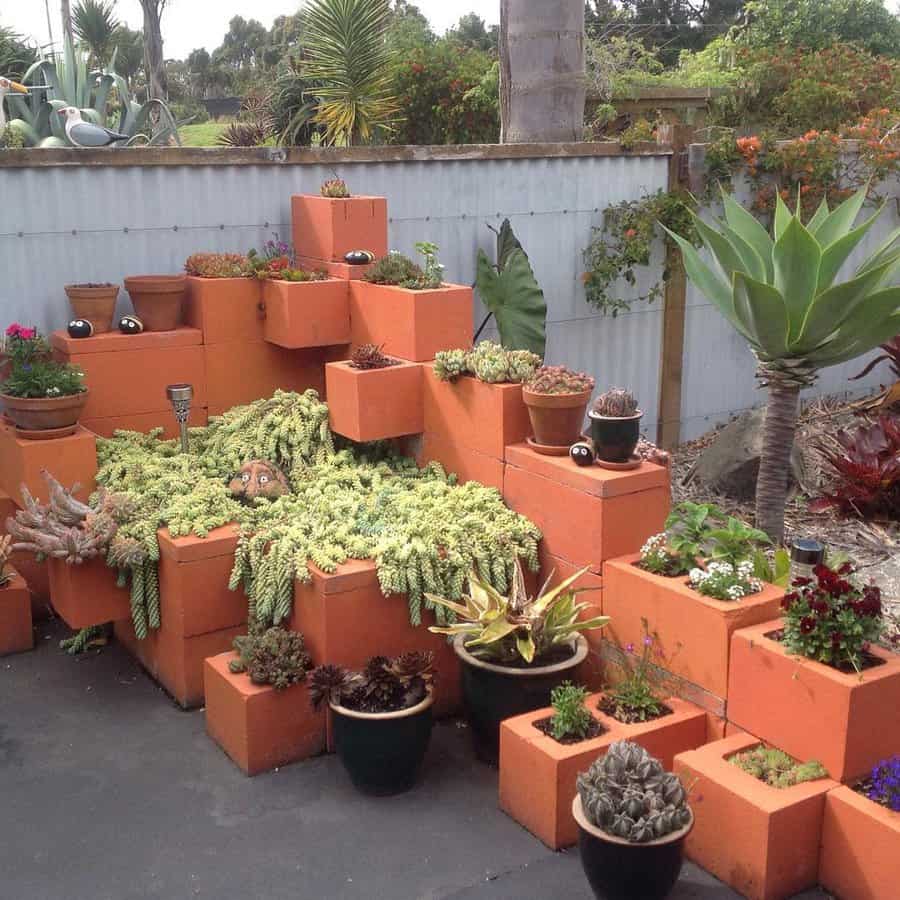 Terracotta planters arranged in a tiered pattern hold various succulents and cacti against a metal fence in an outdoor setting