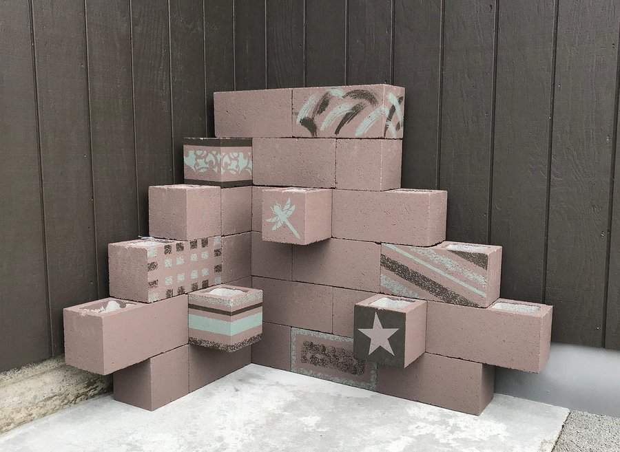 Stacked decorative cinder blocks with various patterns and designs against a dark wooden wall