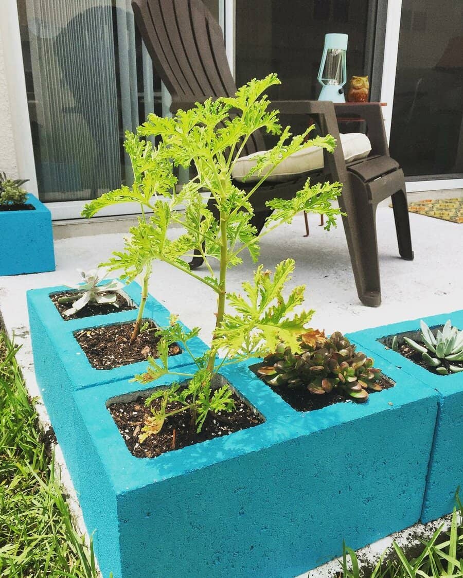 Turquoise cinder blocks with plants, a portable light, and a brown chair on a concrete patio in front of a sliding glass door