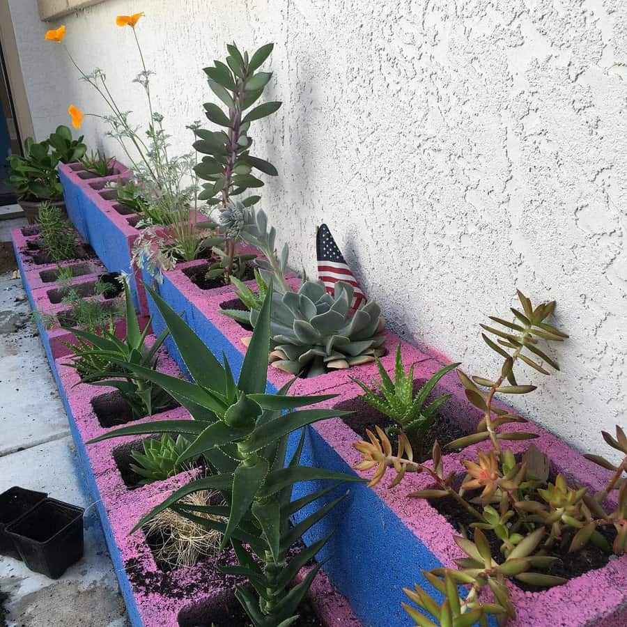 Colorful cinder blocks used as planters with succulents and flowers on a patio, an American flag decoration is visible