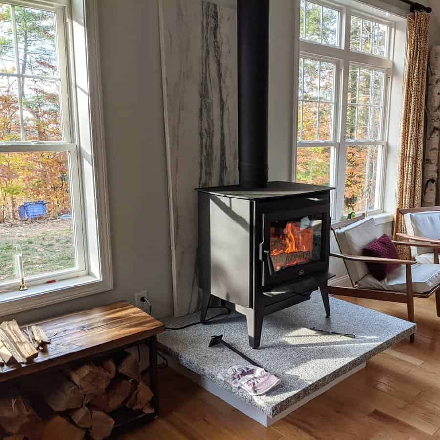 Modern wood stove on a raised stone hearth, set against a marble accent wall with large windows bringing in natural light and autumn views.