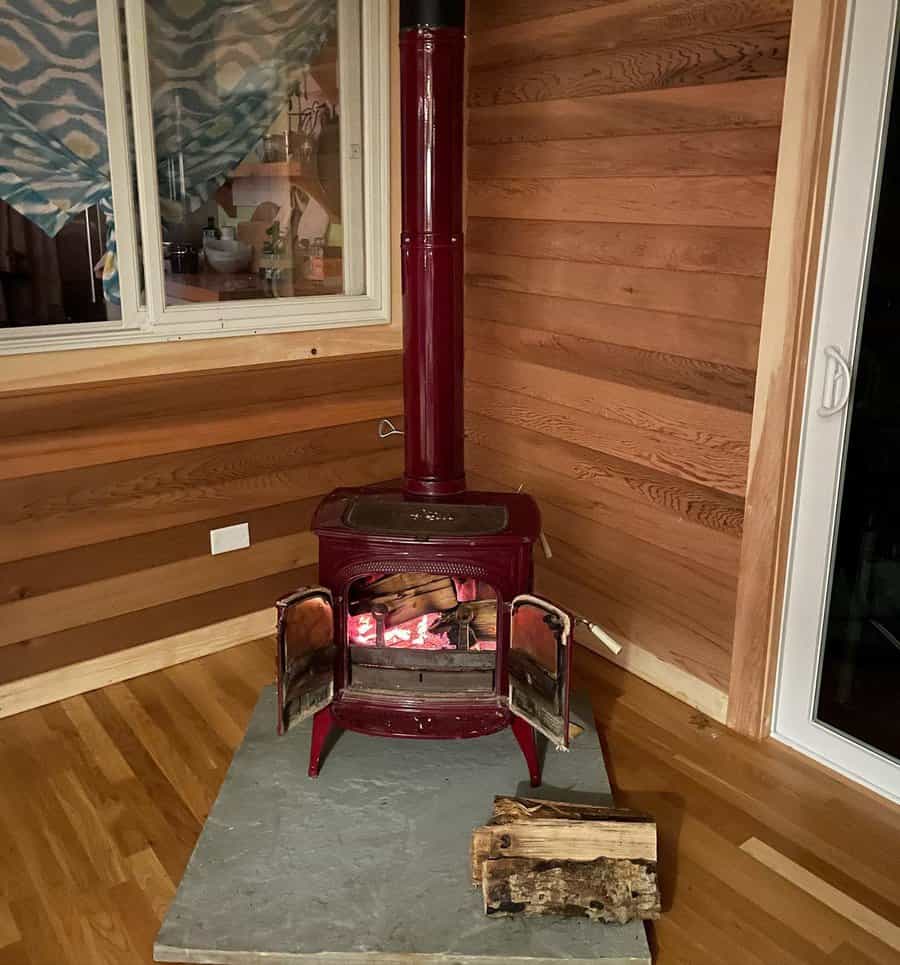 Rustic red cast iron wood stove on a stone hearth, set against warm wooden walls for a cozy and inviting cabin-style ambiance.