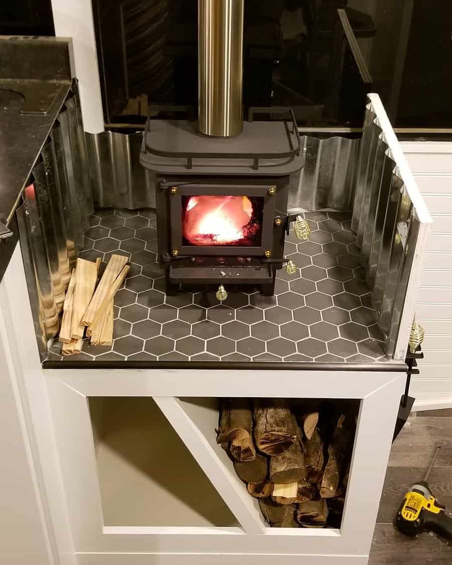 Compact wood stove on a raised hex-tiled hearth with built-in firewood storage and metal heat shields, perfect for a cozy and functional space.