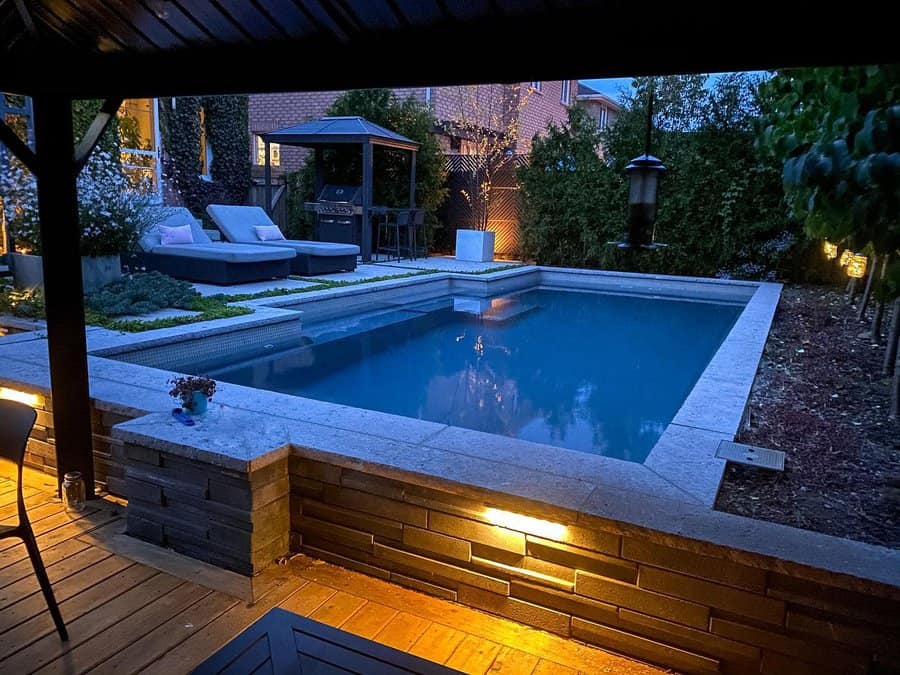 A cozy backyard pool area at dusk with lounge chairs, a small garden, and soft lighting creating a relaxing atmosphere