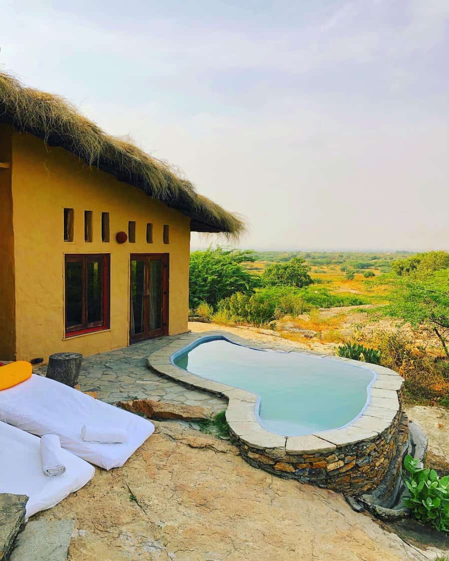 Rural lodge with a small infinity pool overlooking a lush green landscape, next to a stone patio with towels and a lounger