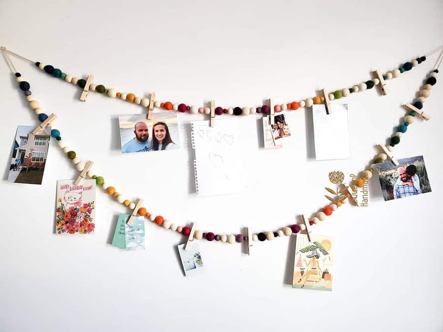 A wall display with two colorful beaded strings, clipped photos, cards, and a paper cutout