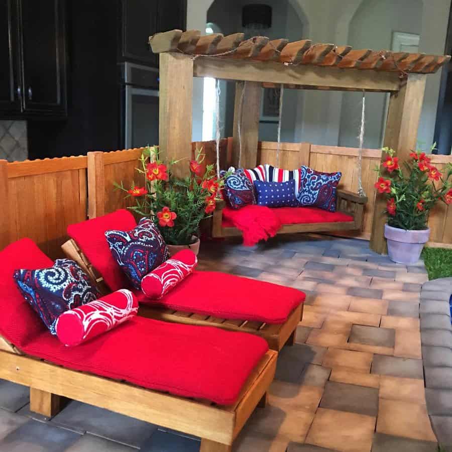 Patio with red-cushioned loungers, wooden swing, colorful pillows, potted plants, and wooden fence on a tiled floor