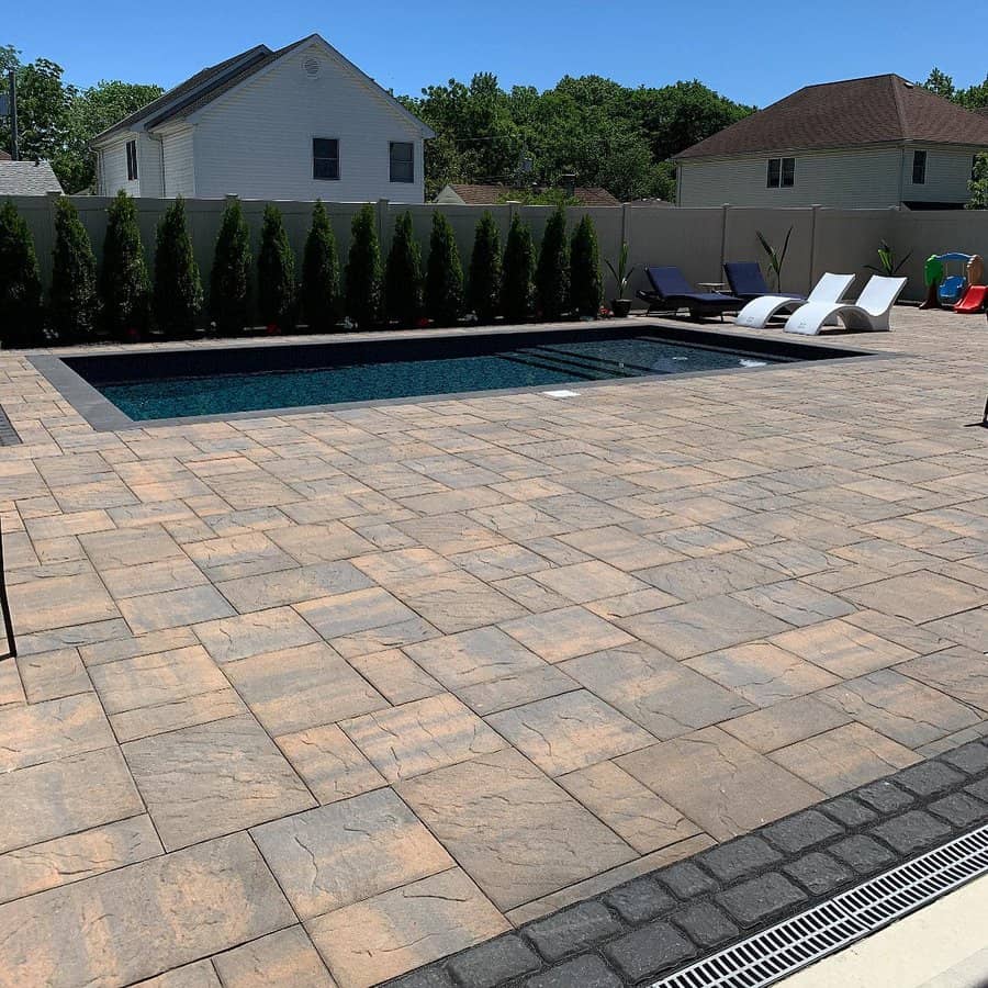 Modern backyard with a sleek in-ground pool, spacious stone paver deck, stylish lounge chairs, and lush greenery for a luxurious outdoor retreat