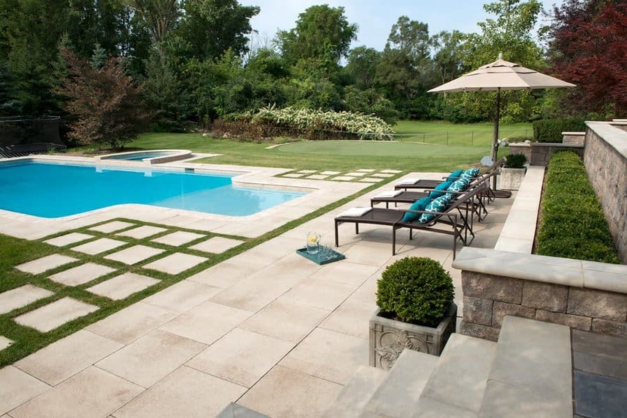 Luxurious backyard pool with large square stone pavers, sleek lounge chairs, a shaded umbrella, and lush greenery for a stylish outdoor retreat