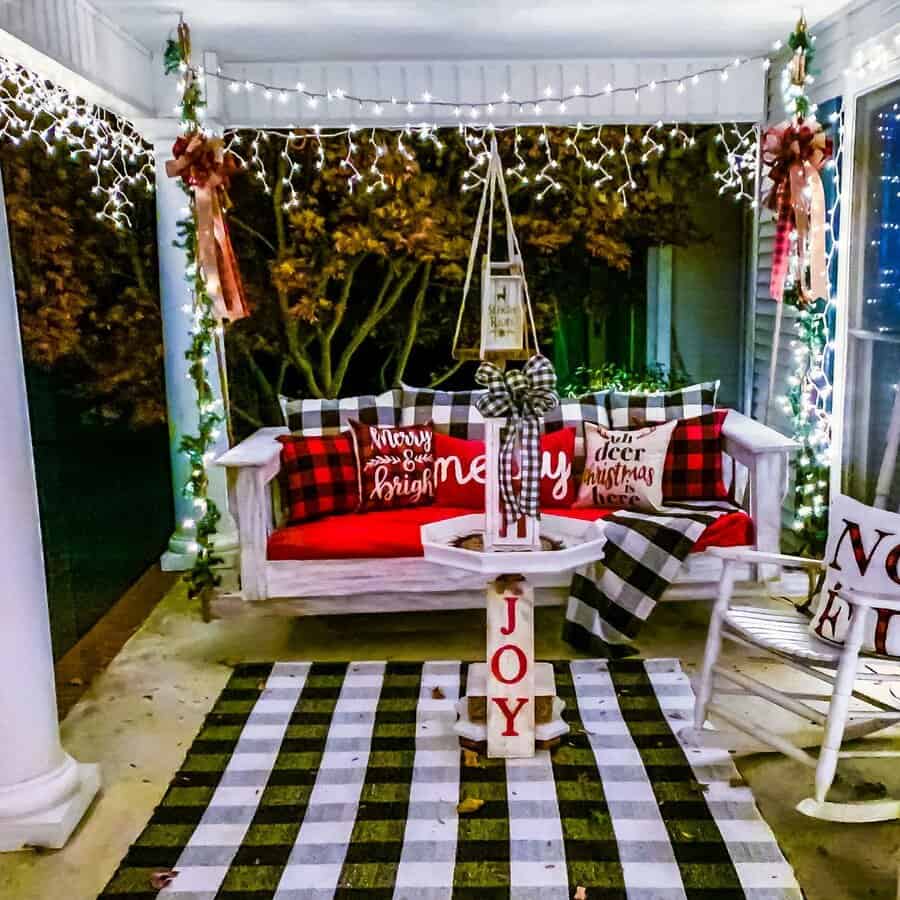 Outdoor porch decorated for Christmas with lights, pillows, and a plaid theme