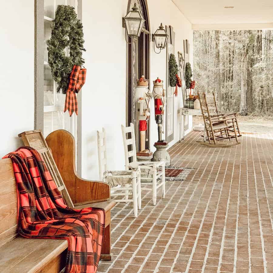 A porch with rocking chairs, wreaths, and plaid blanket on a wooden bench