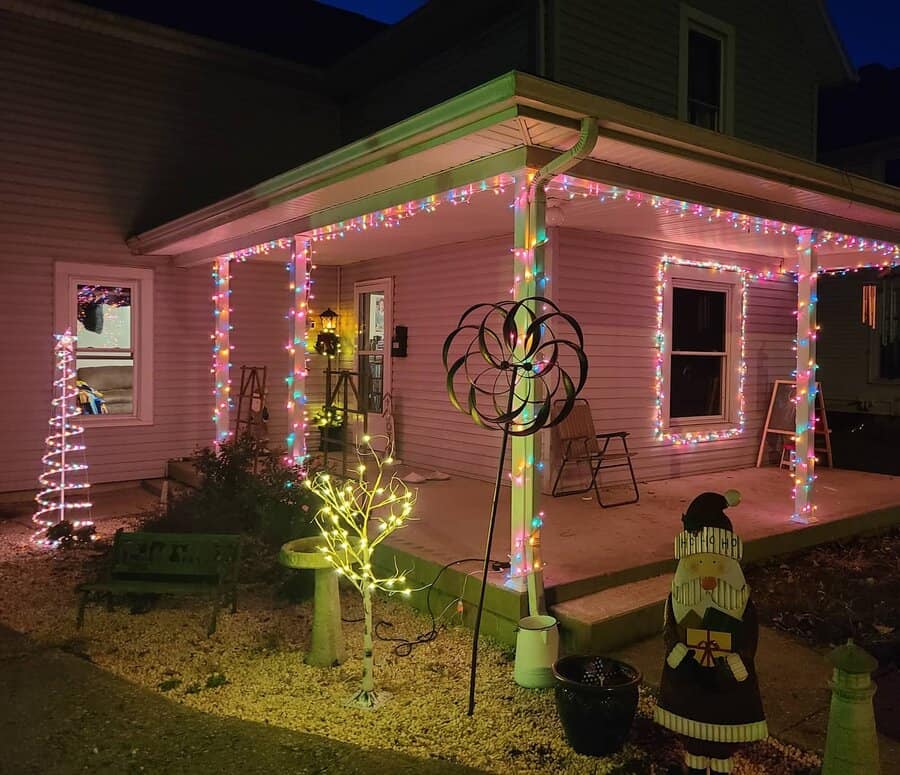 House with a porch decorated in colorful string lights and Christmas ornaments, including a lit tree sculpture and Santa decoration