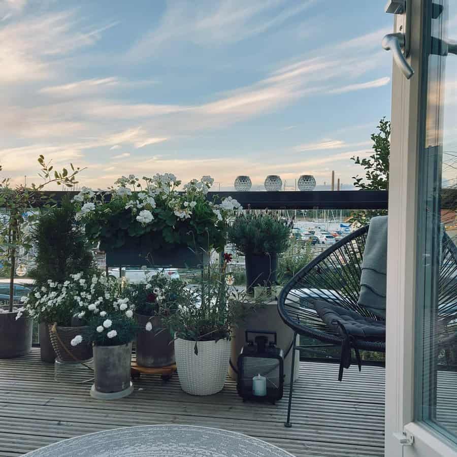 Stylish balcony garden with potted white flowers, a cozy black chair, and a scenic marina view under a soft sunset sky