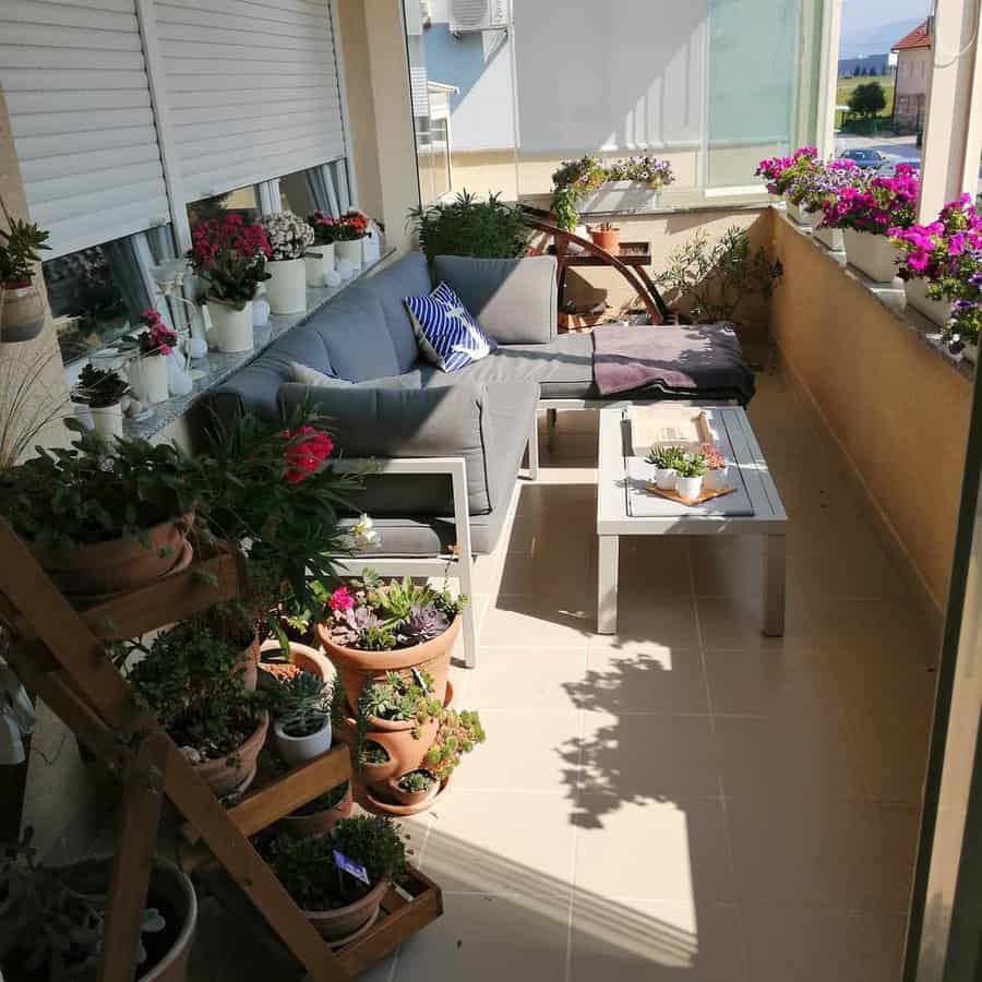 Balcony with gray patio furniture, potted plants, flowers, and a wooden plant stand bathed in sunlight