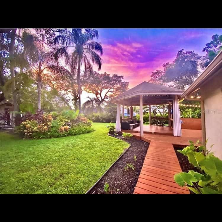 Stunning Florida backyard with a tropical gazebo, lush greenery, and palm trees, set against a breathtaking sunset sky for a serene outdoor escape