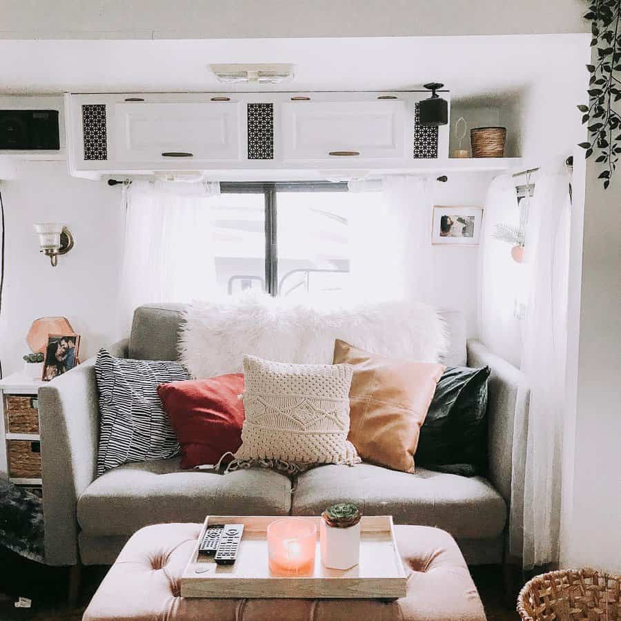 Cozy RV living room with a soft gray sofa, textured pillows, sheer curtains, and a tufted ottoman, creating a warm and inviting small-space retreat