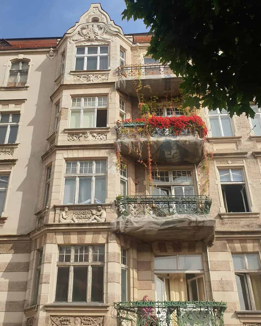 Historic building facade with ornate balconies adorned with red flowers and greenery, under a clear blue sky