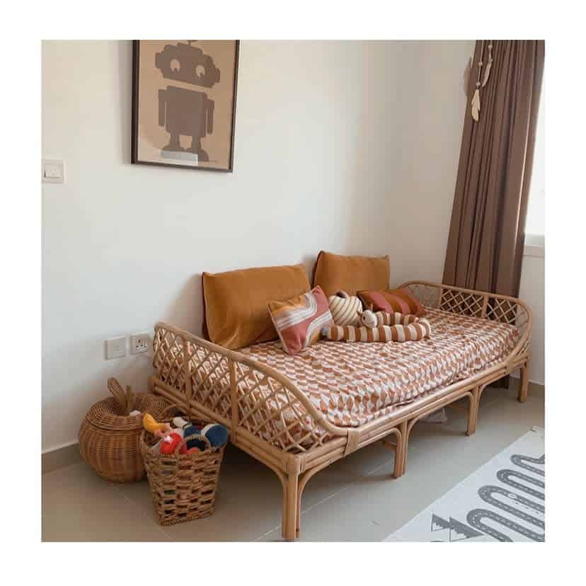 Rattan daybed with brown cushions and striped pillows, a framed robot picture, and woven baskets in a cozy room