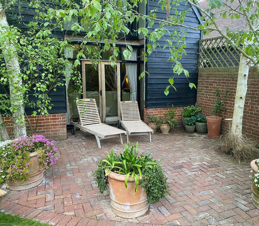 Cozy brick patio with loungers and potted plants by a home