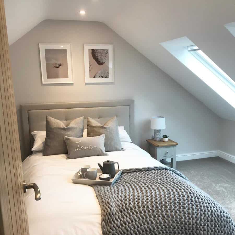 Cozy attic bedroom with soft neutral tones, skylights, and a plush upholstered bed. Warm lighting and textured decor create a serene retreat.