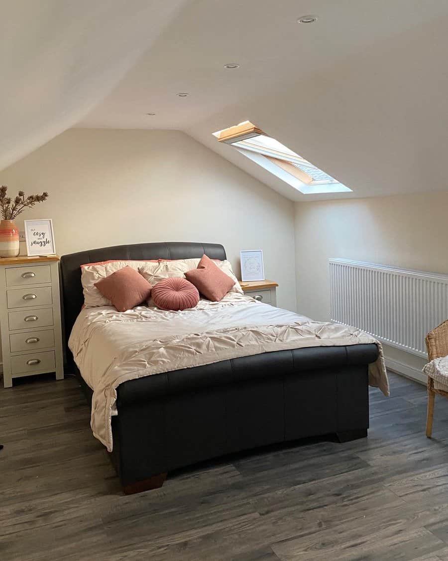 Attic bedroom with a skylight, soft blush accents, and a cozy black bed frame, creating a warm and airy retreat with natural light.