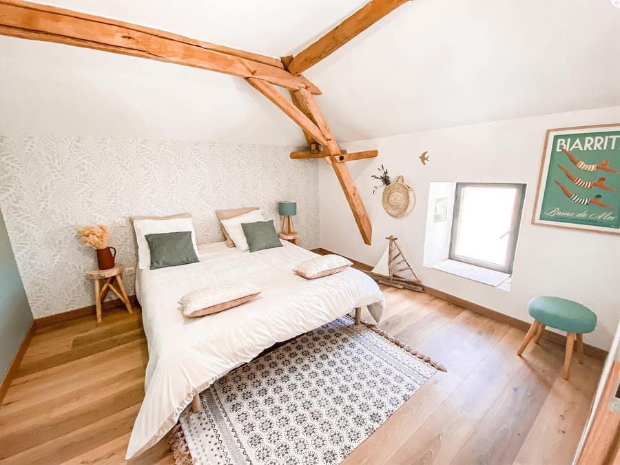 Rustic attic bedroom with exposed wooden beams, soft neutrals, and cozy textures, creating a serene retreat with a touch of vintage charm.