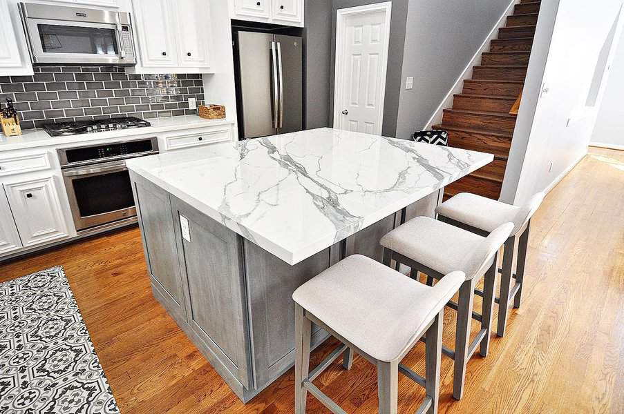 Modern kitchen with marble island, stools, stainless steel appliances, and wooden stairs