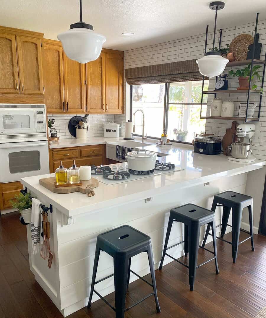 Modern farmhouse kitchen with wooden cabinets, white island, black bar stools, open shelving, and stylish pendant lighting