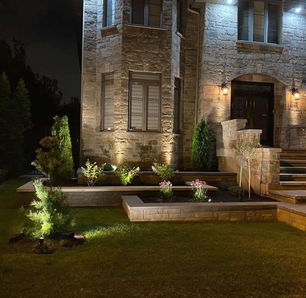 Elegant stone house exterior at night with illuminated retaining walls, garden beds, and pathway lighting