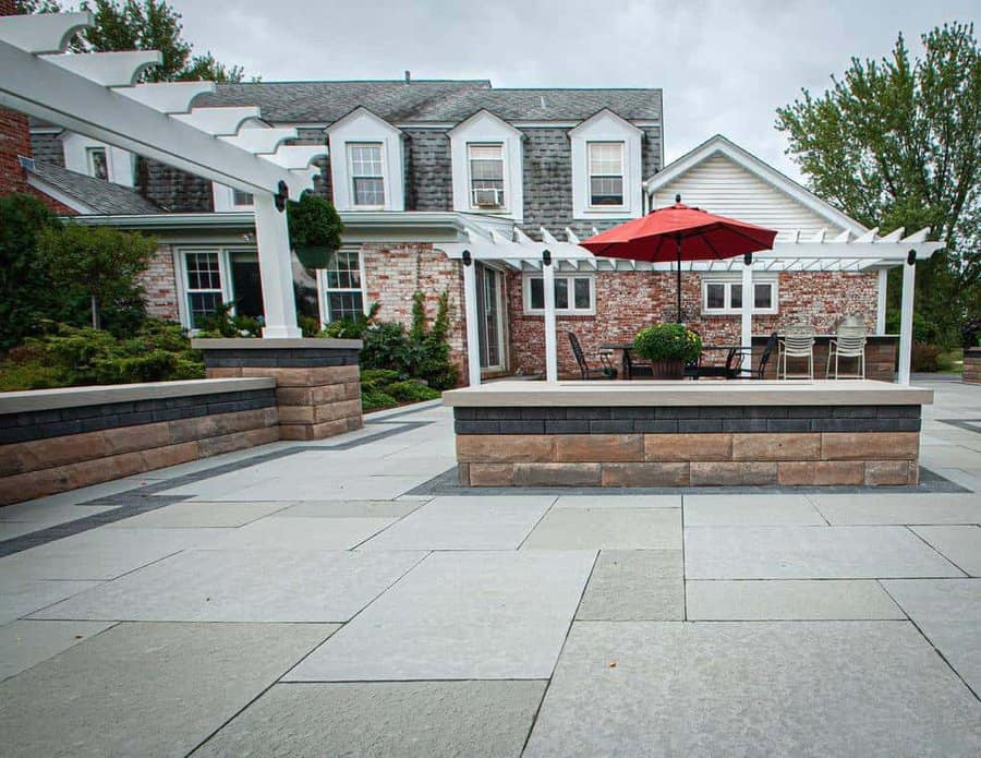 Backyard patio with stone retaining walls, pergola, and outdoor seating area featuring a red umbrella