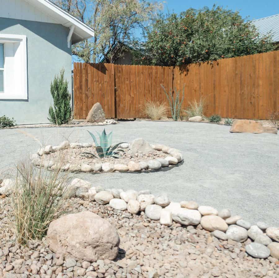 Desert-inspired landscape with gravel ground cover and a central succulent surrounded by a ring of smooth rocks. Drought-tolerant plants and natural boulders create a serene, low-maintenance yard ideal for arid climates.