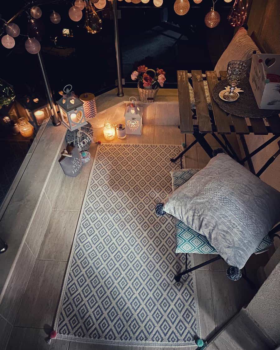 Cozy small balcony at night with a wooden folding table, cushions, and a patterned rug. Warm candlelight and string lights create a romantic and inviting atmosphere.