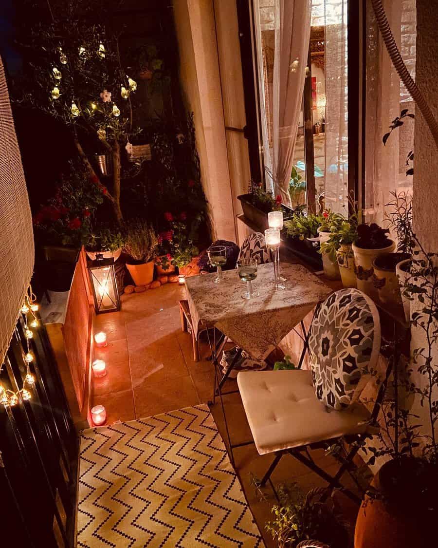 Cozy and romantic small balcony at night with a table set for two, surrounded by candles, fairy lights, and lush greenery. A patterned rug and elegant cushions add warmth to the intimate ambiance.