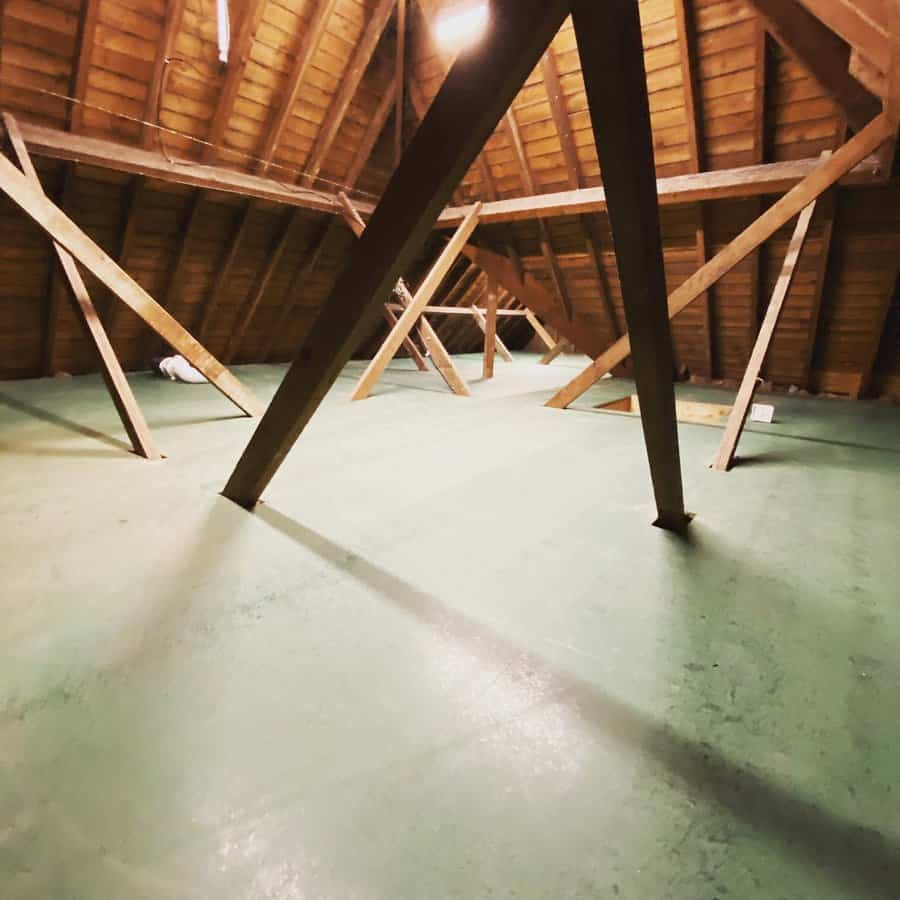 Spacious attic storage area with a sturdy green floor, exposed wooden beams, and ample space for organization under a pitched roof.