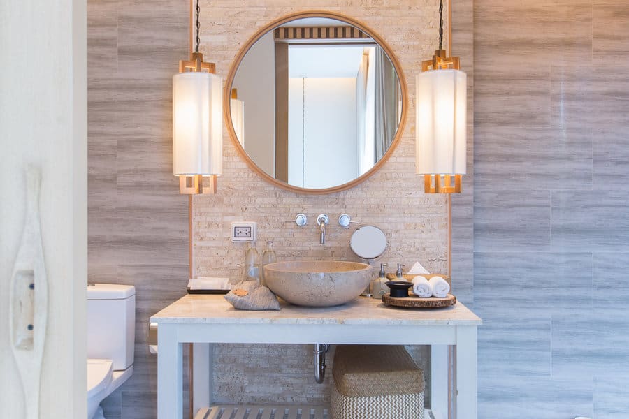 Modern bathroom with a round mirror, stone basin, and pendant lights featuring a textured wall and basket underneath the sink