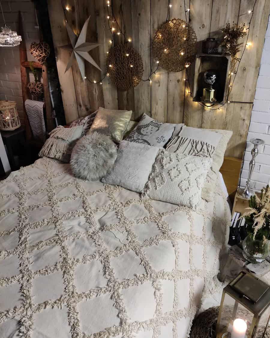 Rustic bedroom with a beige textured bedspread, multiple cushions, wooden wall decor, and string lights creating a warm ambiance