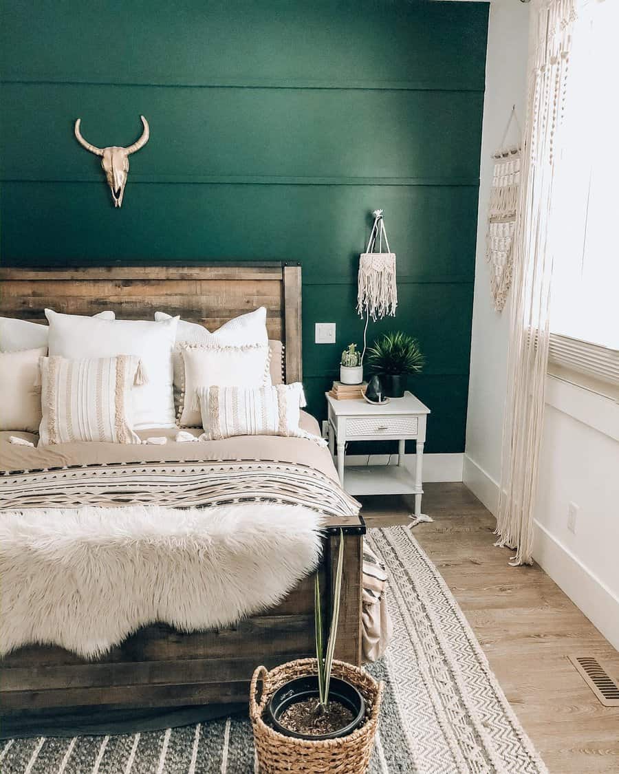 Cozy bedroom with green accent wall, wooden bed, white and beige bedding, macramé wall hanging, and decorative plants