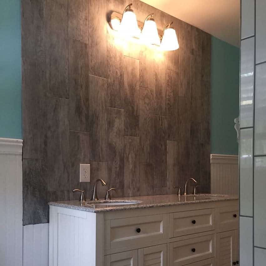 Rustic bathroom with wood-look tile backsplash, double cream vanity, granite countertop, and warm overhead lighting.