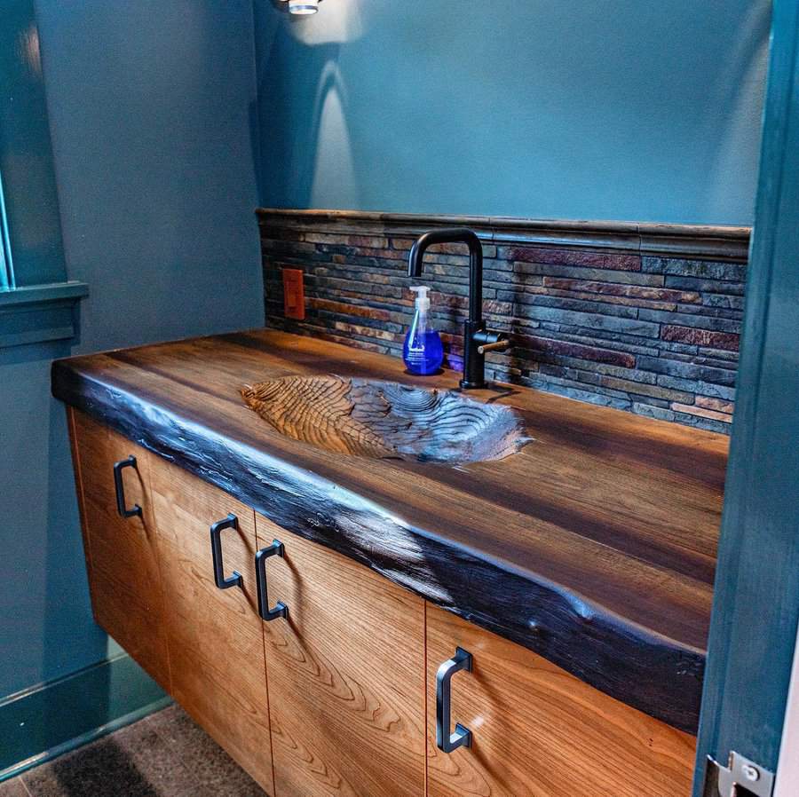 Rustic bathroom with stacked stone backsplash, live-edge wood countertop and integrated sink, paired with a matte black faucet.