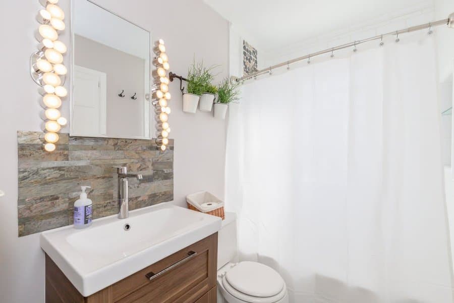 Bright bathroom with wood-look tile backsplash, modern white sink, wood vanity, and playful hanging lights around the mirror.