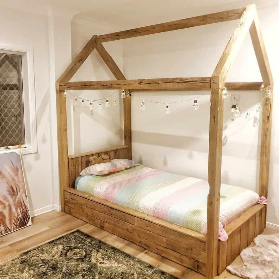 Wooden canopy bed with string lights, a pastel-striped comforter, and a green rug in a cozy room