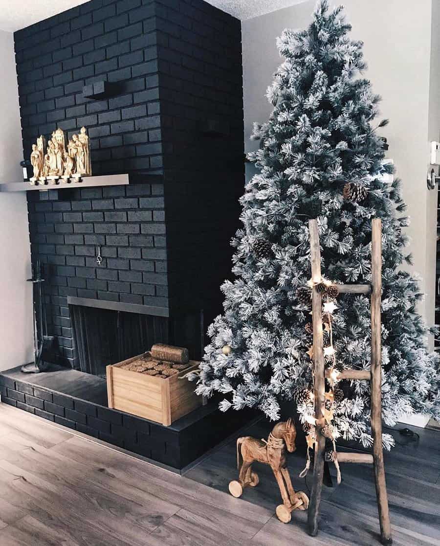 Snowy Christmas tree next to a fireplace with black bricks, wooden ladder, and decor