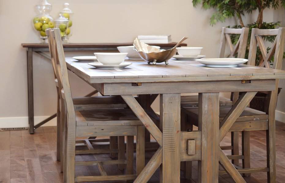 Rustic wooden dining table set for five with white dishes, a decorative centerpiece, and a green plant in the background