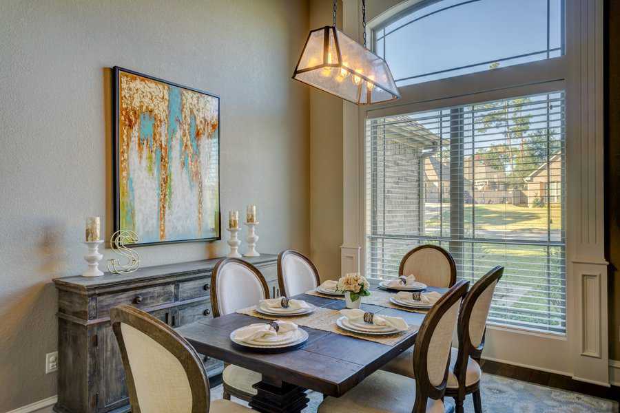 Dining room with a dark wood table set for four, large window with blinds, chandelier, abstract painting, and outside view