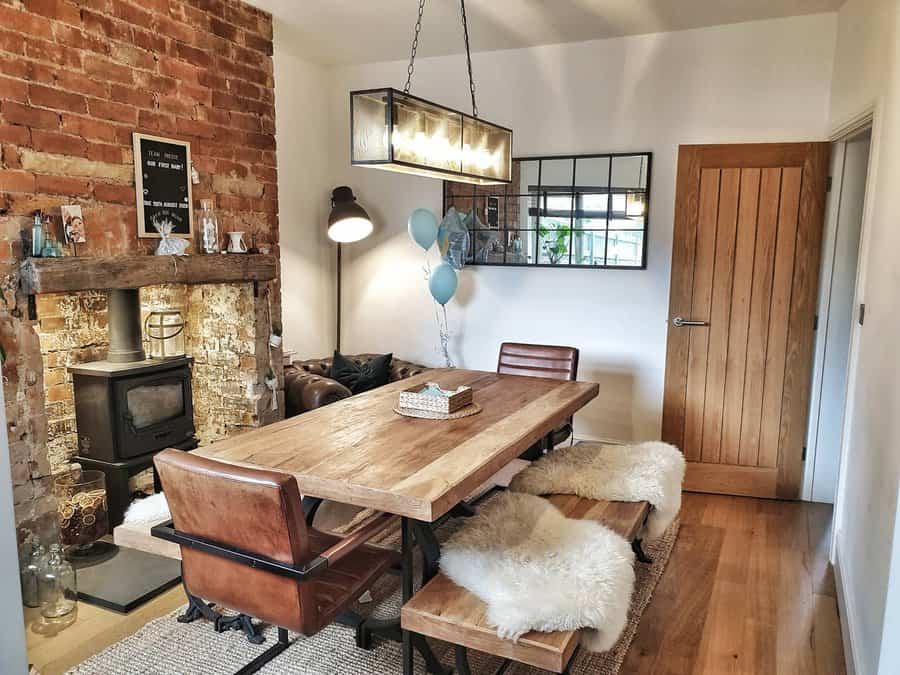 Cozy dining room with a wooden table, leather chairs, a fireplace, exposed brick wall, and modern lighting