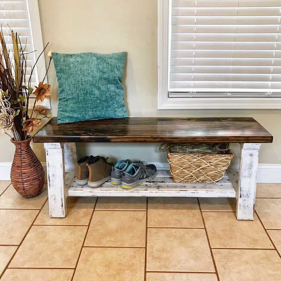 Rustic entryway with a distressed wood bench, shoe storage, a woven basket, and a teal accent pillow, blending function with farmhouse charm